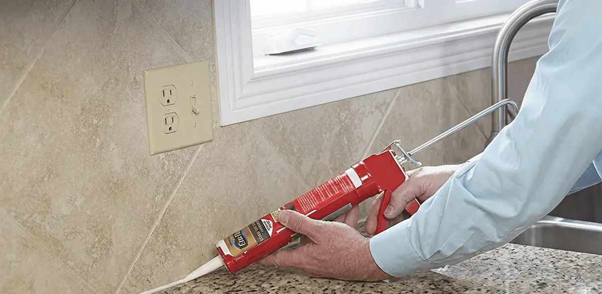 Handyman applying caulk along a kitchen backsplash and countertop seam in Boston, MA