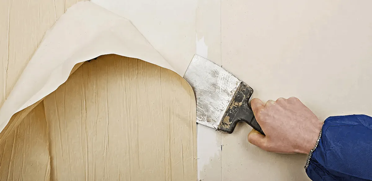 Handyman removing wallpaper with a scraper for wall preparation in Boston, MA