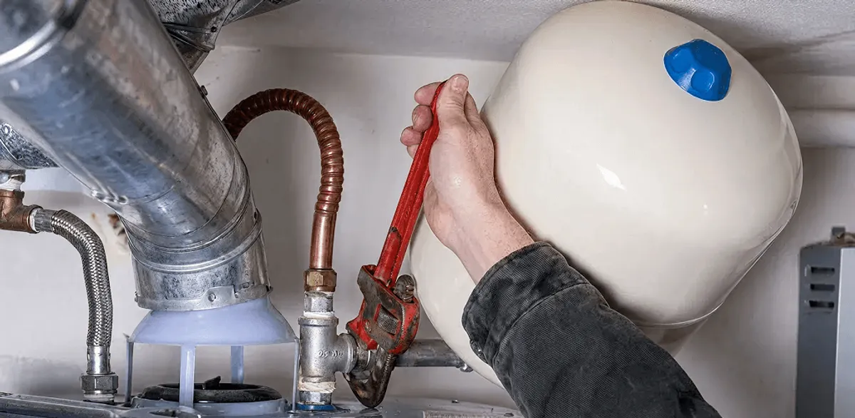 Water heater repair technician tightening plumbing connections near a tank unit in Boston, MA